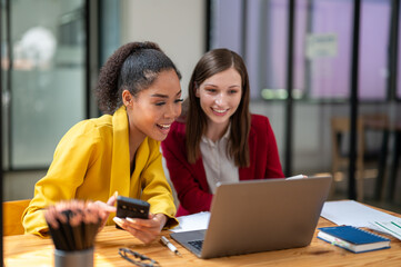 A businesswoman in a yellow blazer engaging in a productive discussion with a colleague in a red jacket over work documents in an office.