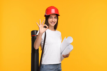 Architect in hard hat with drafts and tube showing ok gesture on yellow background
