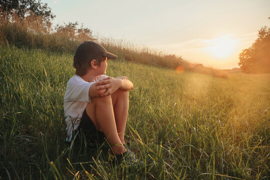 Happy boy sitting on grass field wearing white t-shirt, sunset