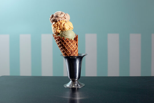 three scoops of ice cream in a waffle cone against striped background