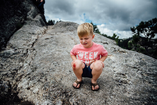 Wide view of little boy sitting on rocks and crying with skinned knee.
