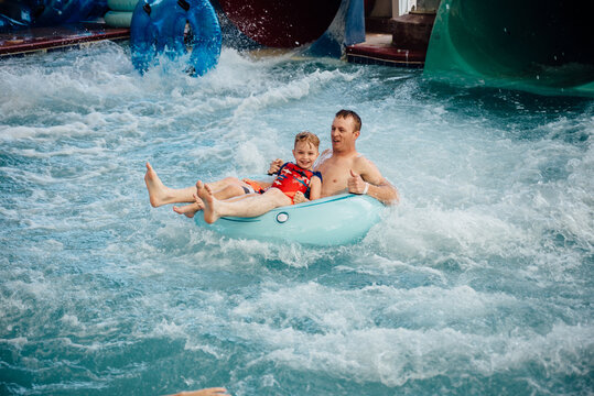 Wide view of smiling dad and son on inner tube at indoor water park.