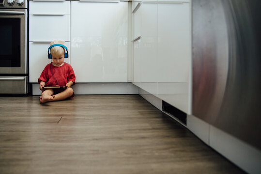 Wide view of boy with tablet and headphones sitting in kitchen