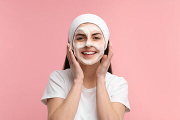 Young woman with headband washing her face on pink background