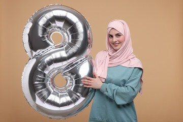 Happy Women's Day. Woman in hijab with balloon in shape of number 8 on beige background
