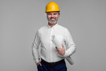 Architect in hard hat holding draft on grey background