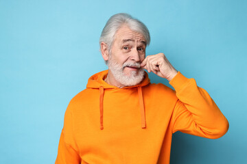 Senior man touching mustache on light blue background