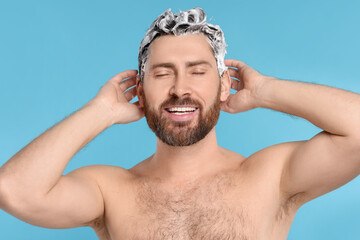 Happy man washing his hair with shampoo on light blue background