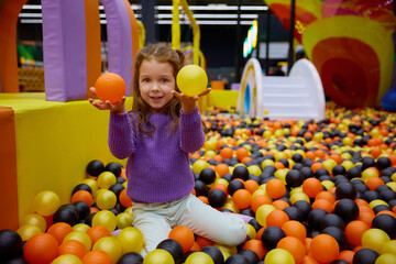 Portrait of funny little girl child playing in ball pit - 780340777