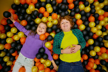 Charming funny children lying in dry pool with colorful balls - 780340979