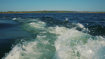 A trail of water on a lake seen behind a speeding motorboat on a clear day, the surface of the water