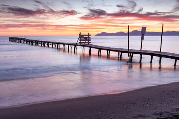 Beautiful sunrise on a beach with old wooden jetty in Platja de Muro, Majorca, Balearic Islands, Spain