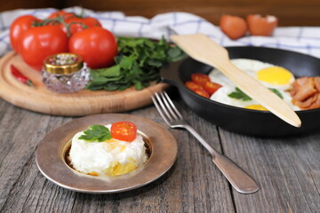 On a wooden table is a plate with fried egg, tomato and greens.