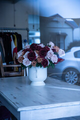 Vase of flowers on a table in a shop with reflections of the outside world in the window