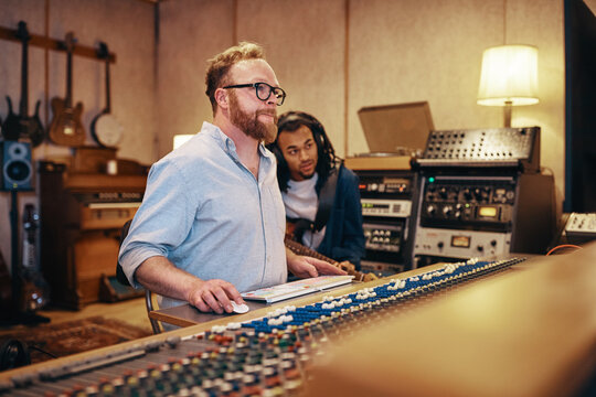 Producer and a young black charismatic guitarist with dreadlocks, working on tracks in a recording studio.