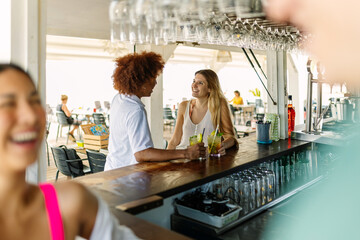 Diverse young people enjoying a mojito drink during happy hours while hanging out at beach bar. Travel and vacation concept.