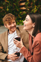 A man and a woman sit side by side, clinking wine glasses in a romantic gesture