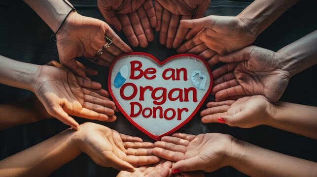 United for Organ Donation. Multiple hands form a circle around a heart-shaped cushion with "Be an Organ Donor" text, promoting unity in the organ donation movement
