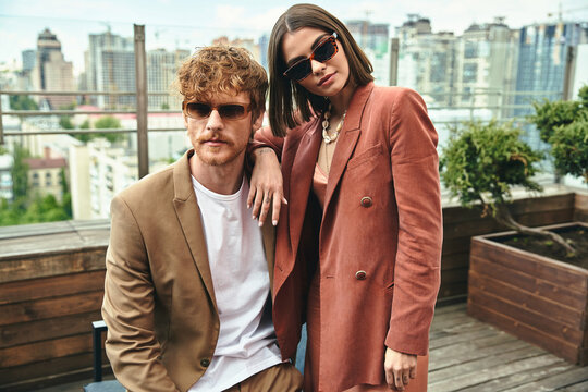 A stylish man and woman striking a pose together, exuding elegance and charm in a picturesque setting