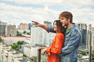 A man and a woman standing confidently on the rooftop of a building, looking out at the city...