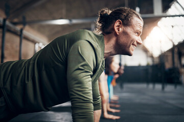 Smiling man doing push-ups during a workout class at the gym. His friends next to him are also doing push ups.