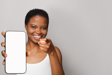 Positive healthy woman holding smartphone with white empty blank screen display on gray studio wall...