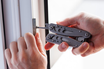 A man's hands fixing the window frame with a multitool