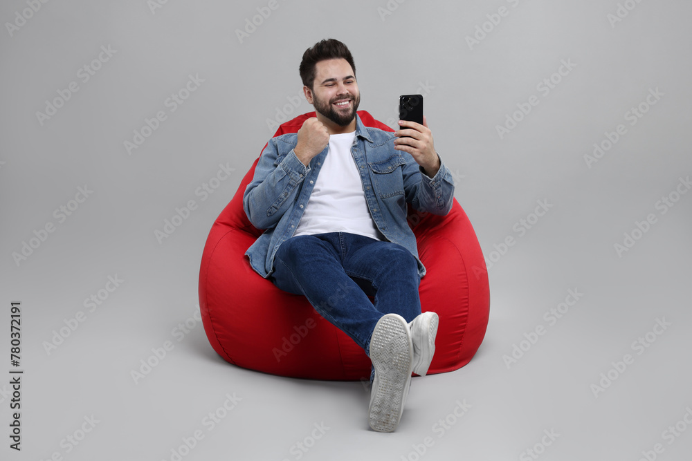 Canvas Prints Happy young man using smartphone on bean bag chair against grey background