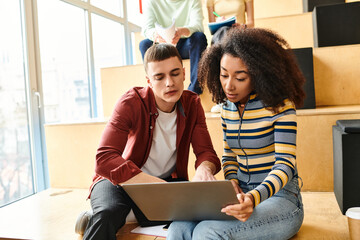 A black girl and a man sit on the floor, focused on a laptop screen, engaged in collaborative learning