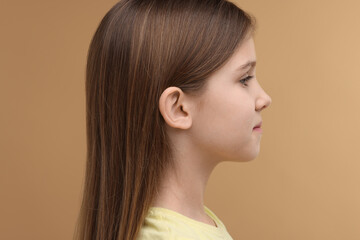 Hearing problem. Little girl on pale brown background