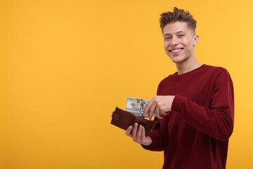 Happy man putting money into wallet on yellow background. Space for text