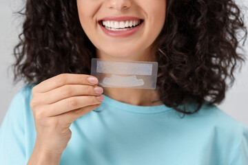 Young woman holding teeth whitening strips on light background, closeup
