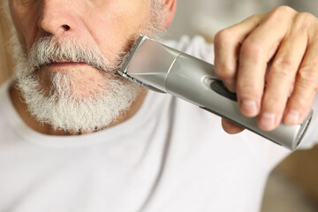 Man trimming beard with electric trimmer indoors, closeup - obrazy, fototapety, plakaty