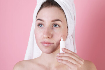 Young woman with acne problem applying cosmetic product onto her skin on pink background