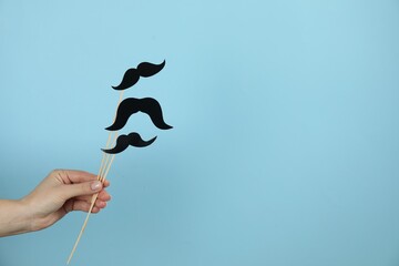 Woman with fake paper mustaches on light blue background, closeup. Space for text