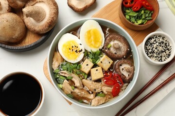 Bowl of delicious ramen and ingredients on white table, flat lay. Noodle soup