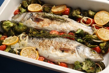 Delicious fish with vegetables and lemon in baking dish on table, closeup