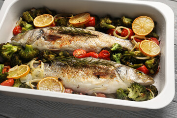 Delicious fish with vegetables and lemon in baking dish on table