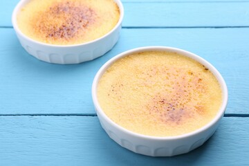 Delicious creme brulee in bowls on light blue wooden table, closeup