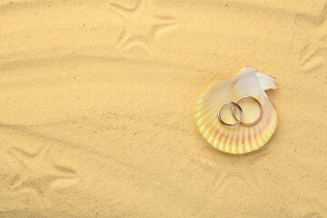 Fototapeta na wymiar Honeymoon concept. Two golden rings with shell on sand, top view. Space for text