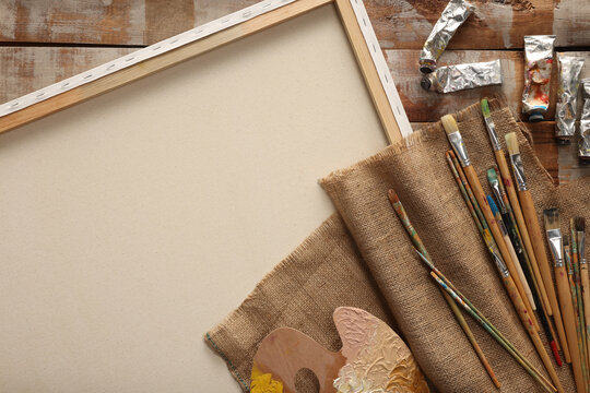 Natural burlap fabric and different painting supplies on wooden table , top view