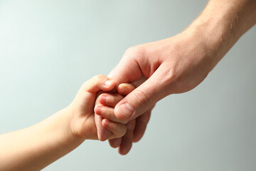 Father and child holding hands on light blue background, closeup