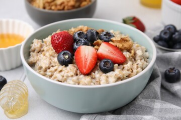 Tasty oatmeal with strawberries, blueberries and walnuts in bowl on grey table, closeup