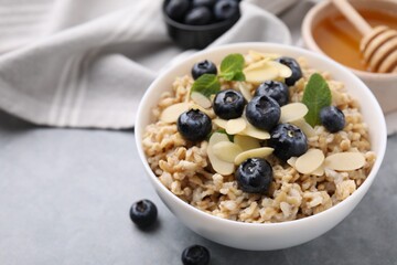 Tasty oatmeal with blueberries, mint and almond petals in bowl on grey table, closeup. Space for text
