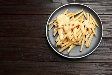 Delicious french fries with cheese sauce on wooden table, top view. Space for text