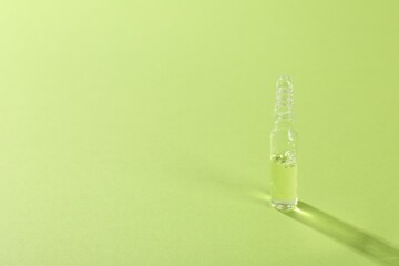 Glass ampoule with liquid on light green background. Space for text