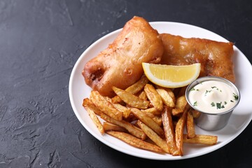 Tasty fish, chips, lemon and sauce on black table, closeup. Space for text