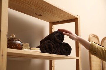 Woman taking rolled towel from shelf indoors, closeup