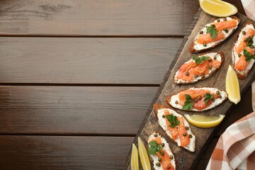 Tasty canapes with salmon, capers, lemon and cream cheese on wooden table, top view. Space for text