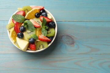 Tasty fruit salad in bowl on light blue wooden table, top view. Space for text